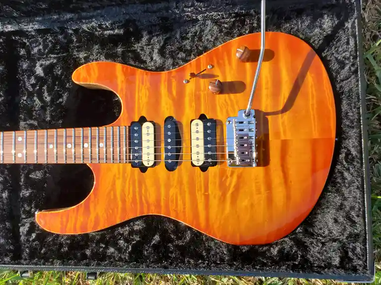 A sunburst-finished electric guitar with a glossy finish and visible wood grain rests inside an open black case lined with…