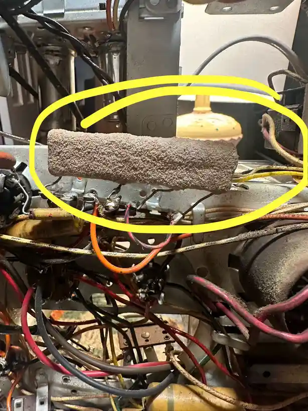 a close-up photo of a messy, tangled mess of old electrical wires and components inside a machine, with a yellow circle…
