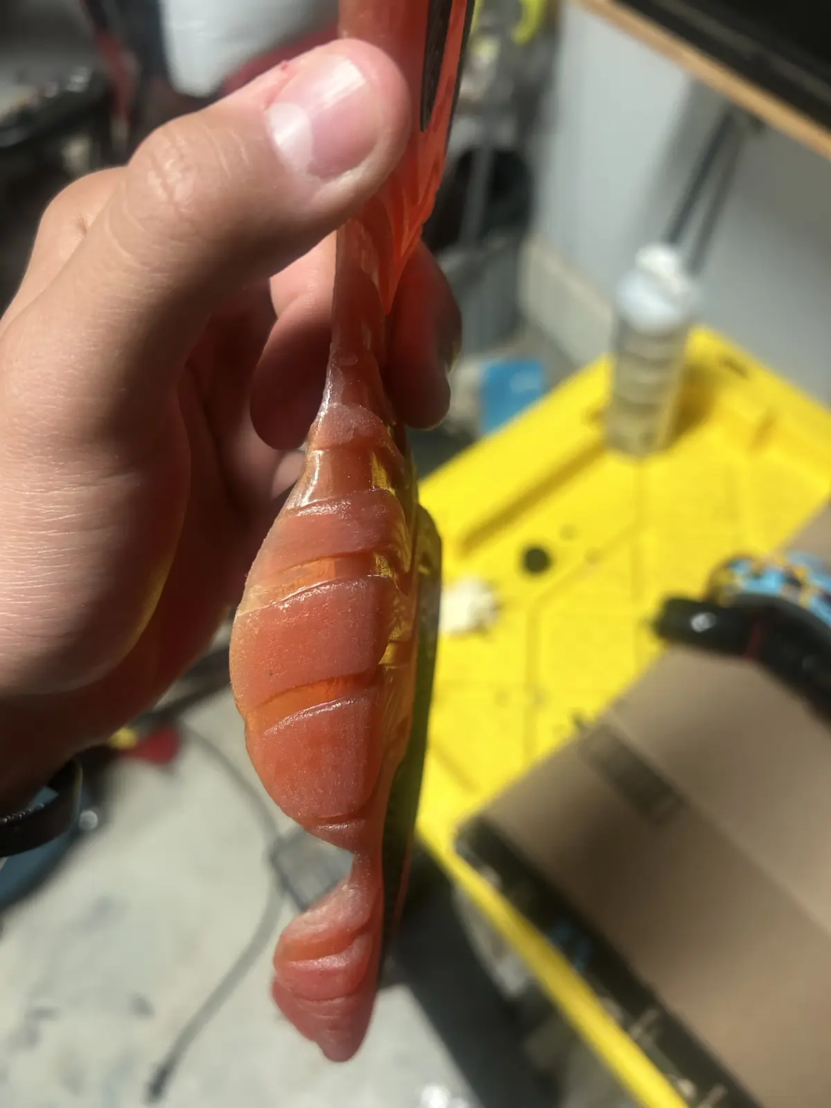 A hand holds a fishing lure shaped and colored like a salmon, with a realistic orange-pink body and segmented texture…