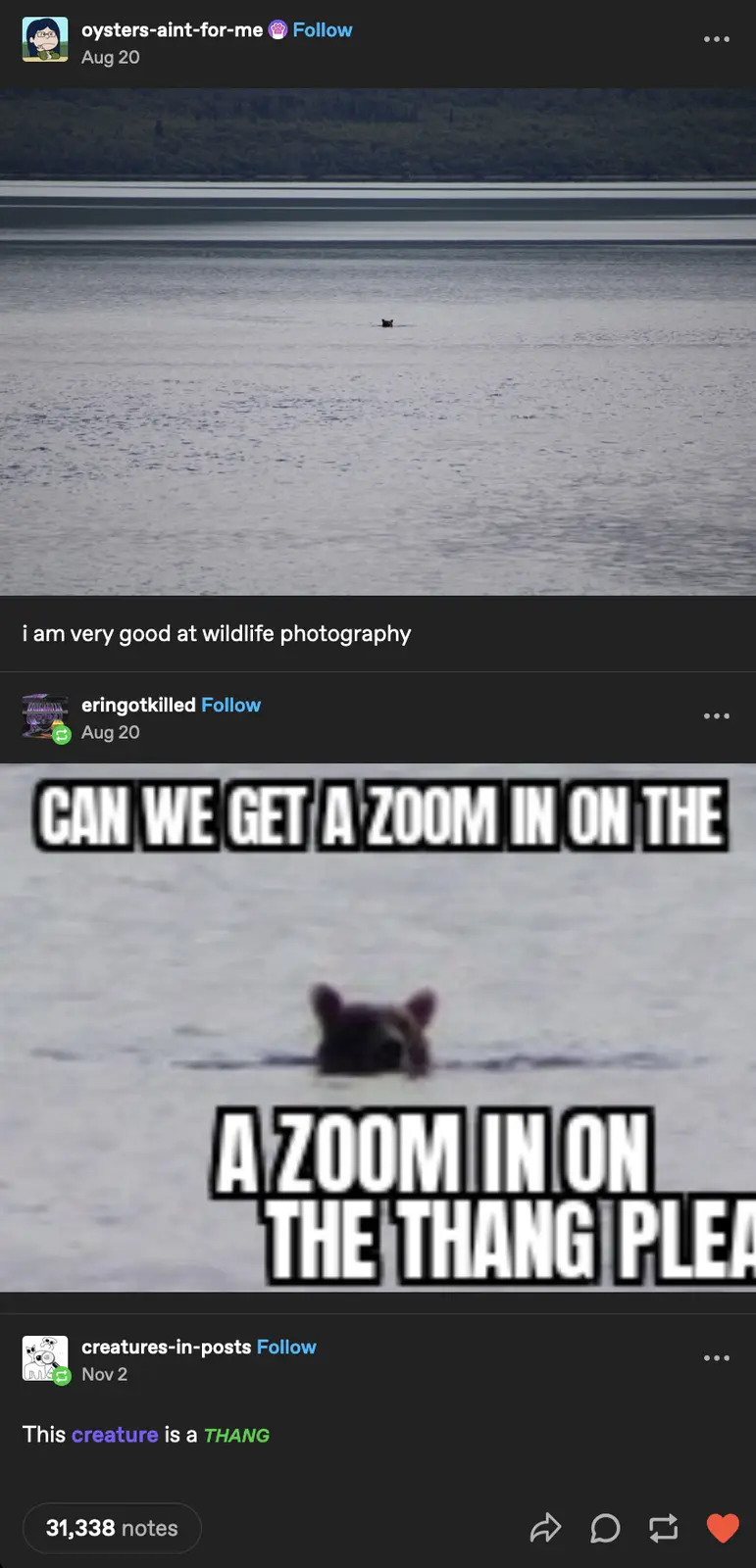 The image shows a distant, blurry view of a dark, small animal partially submerged in water, with a forested shoreline in…