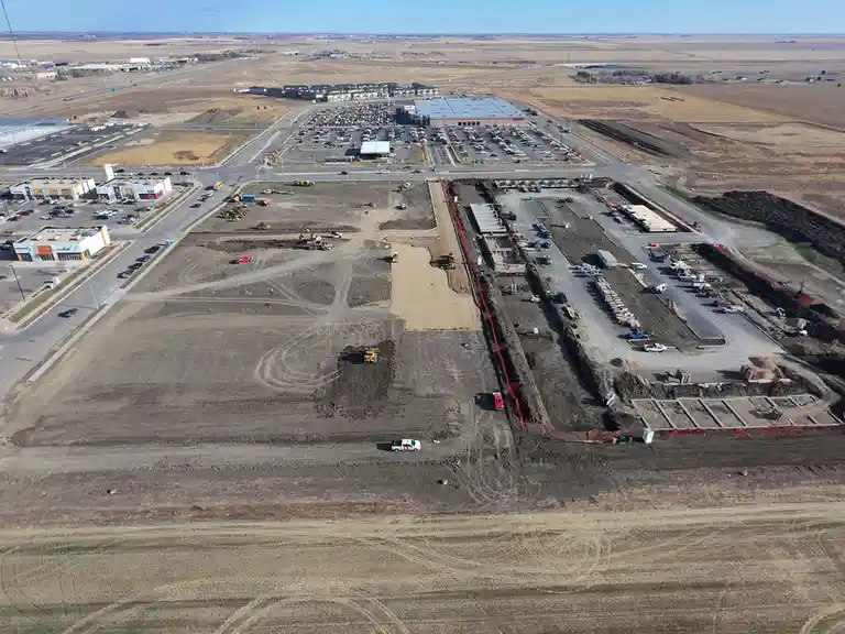 An aerial view shows a large, active construction site with heavy machinery, excavated earth, and partially built…