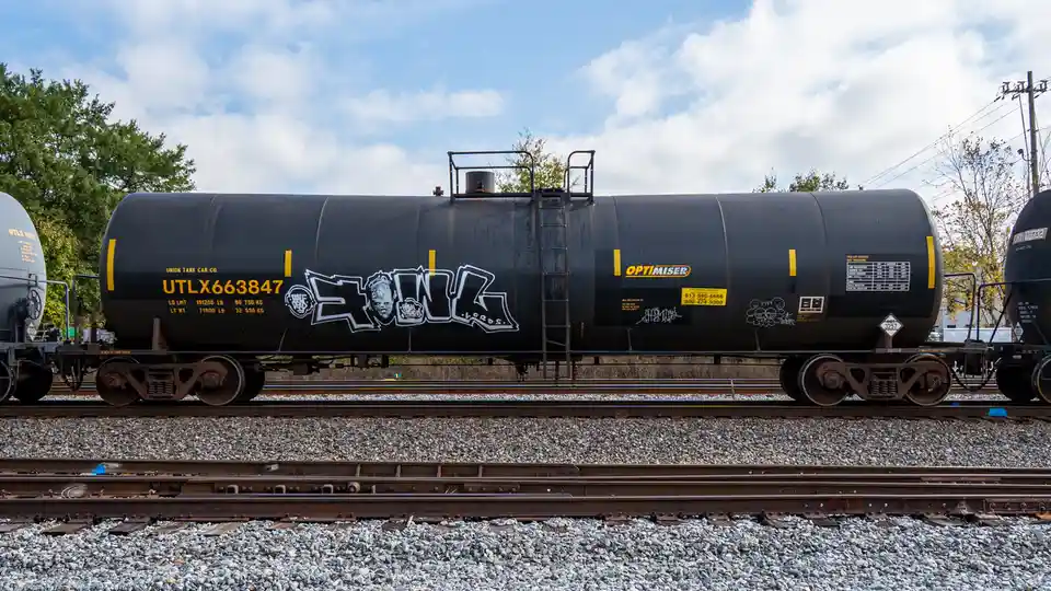 A black Union Tank Car Co. tanker railcar, marked UTLX663847, sits on tracks under a partly cloudy sky. It features…