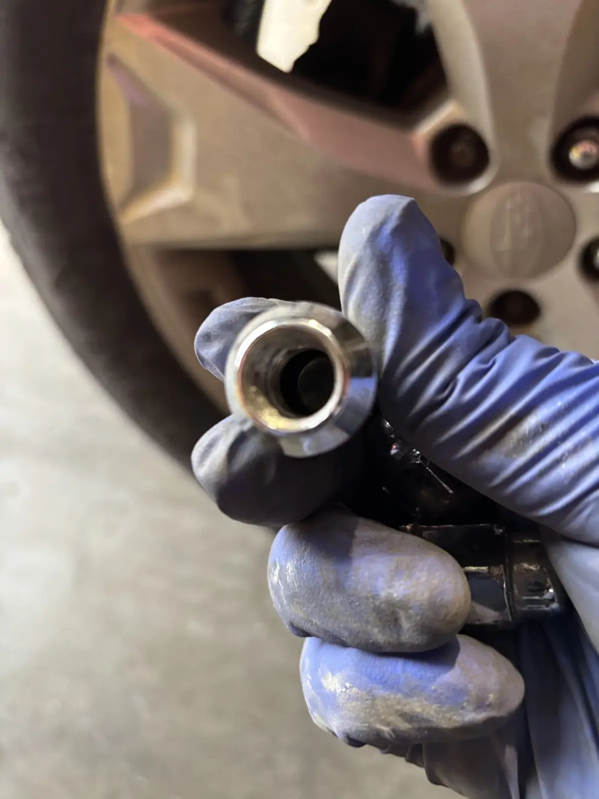 A close-up shot shows a gloved hand holding a shiny, freshly replaced wheel bearing, with a car wheel and hub visible in the…