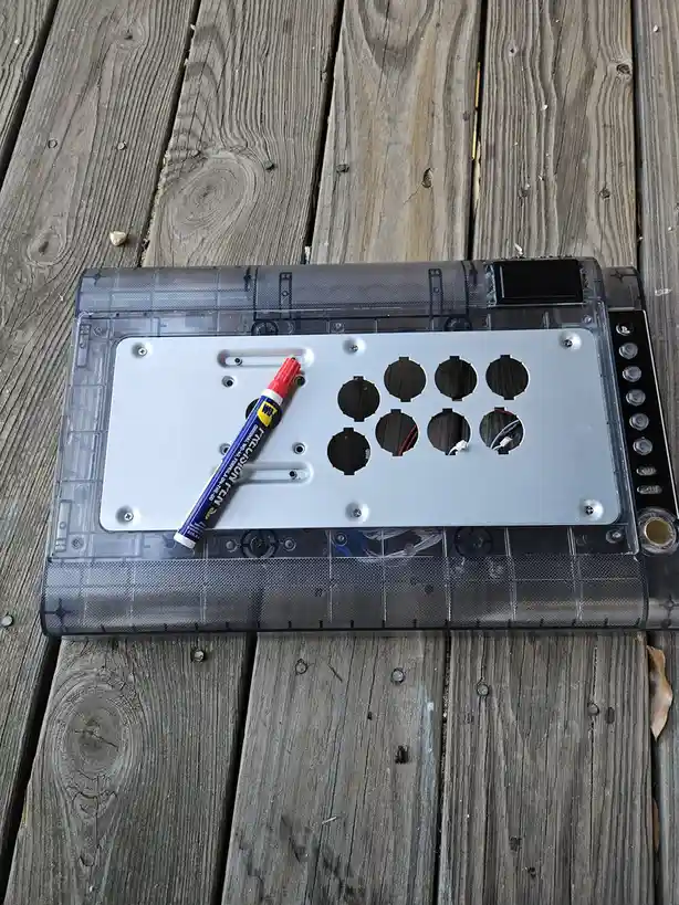 A transparent keyboard case with a silver plate and circular cutouts sits on weathered wooden planks. A red-tipped precision…