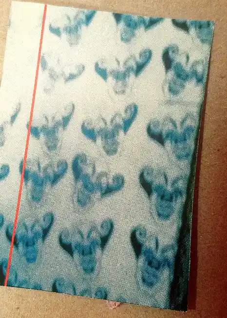 A close-up of a textile with a repeating pattern of blue, abstract, stylized faces or masks on a light background, featuring…