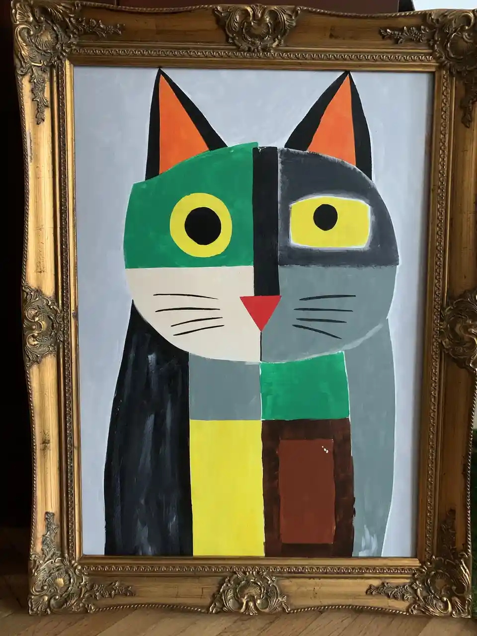 A painting of a stylized cat in a gold ornate frame, split vertically down the middle with contrasting colors and features…