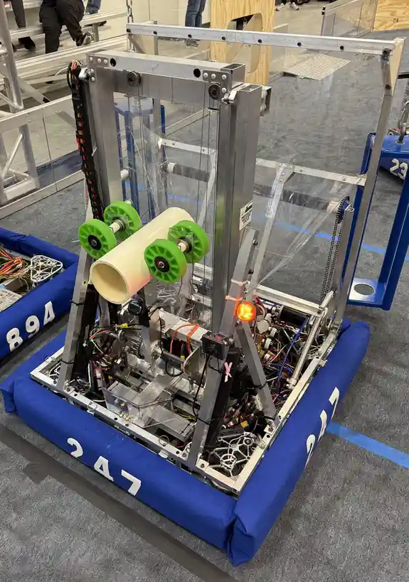 A complex, custom-built robot with a blue padded base marked '247', featuring exposed wiring, gears, and a large white…