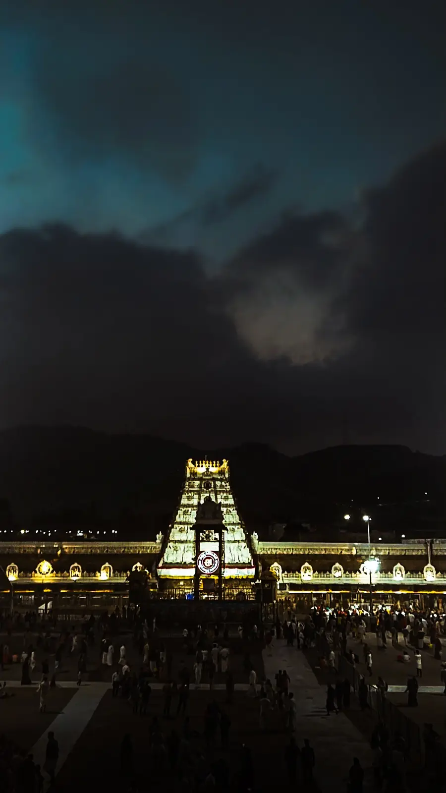 A nighttime photograph of a large, ornate temple with intricate carvings, illuminated by bright lights against a dark sky…