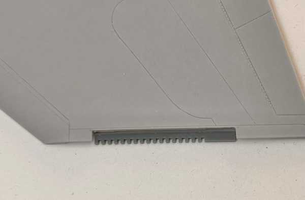 a close-up photo of a gray plastic object, likely part of a model airplane or drone, showing a small rectangular slot with a…