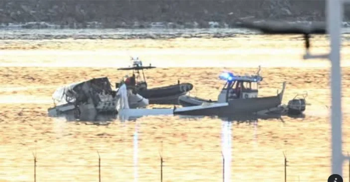A blurry photo shows a damaged boat partially submerged in water, with a police boat nearby flashing blue lights. The…