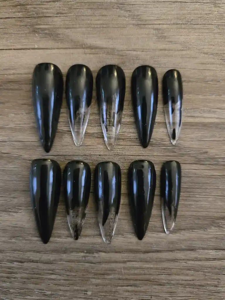 Ten long, pointed, glossy black and clear nail-shaped objects are arranged in two rows on a wooden surface. The text…