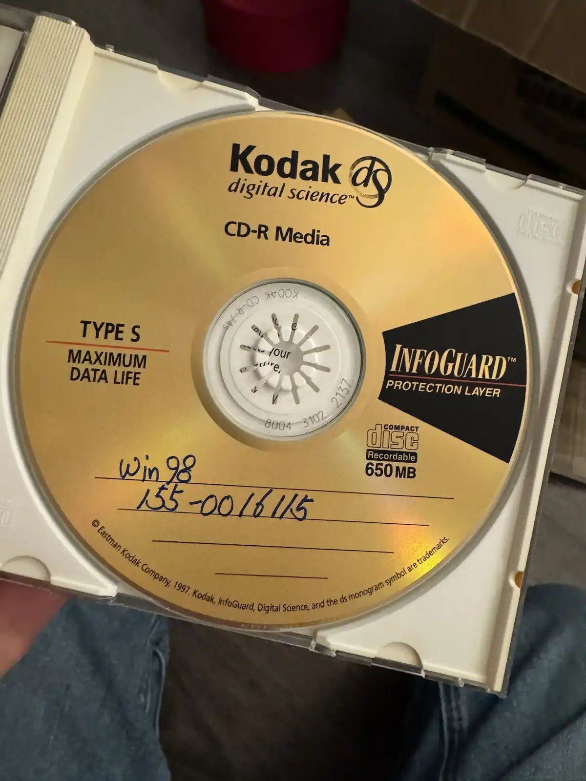 A close-up photo of a gold-colored Kodak CD-R disc in its white plastic case, with handwritten text in blue ink reading 'win…