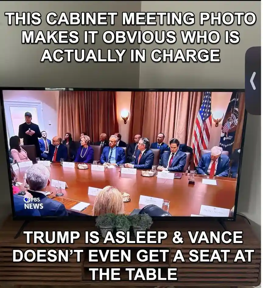 A photo of a television screen showing a cabinet meeting with multiple people seated around a large wooden table. The person…