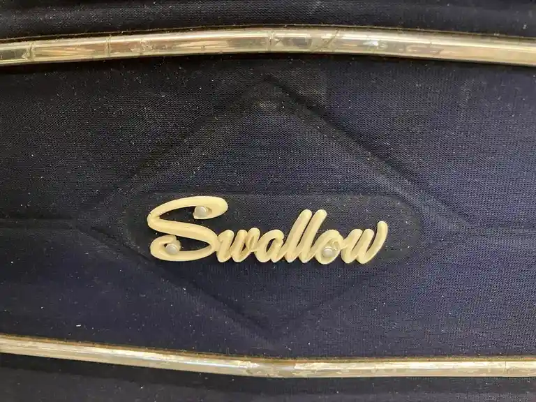 A close-up photo shows a cream-colored, cursive 'Swallow' logo affixed to dark blue fabric, framed by two horizontal…