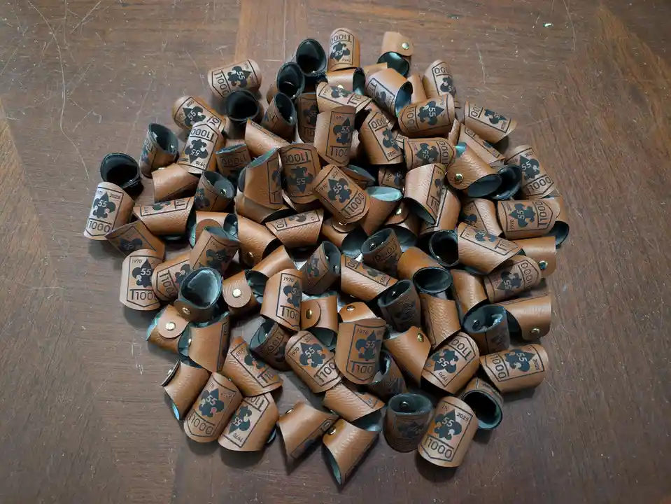 A pile of brown leather wristbands with black ink designs, featuring a fleur-de-lis, the number 55, and the years 1970 and…