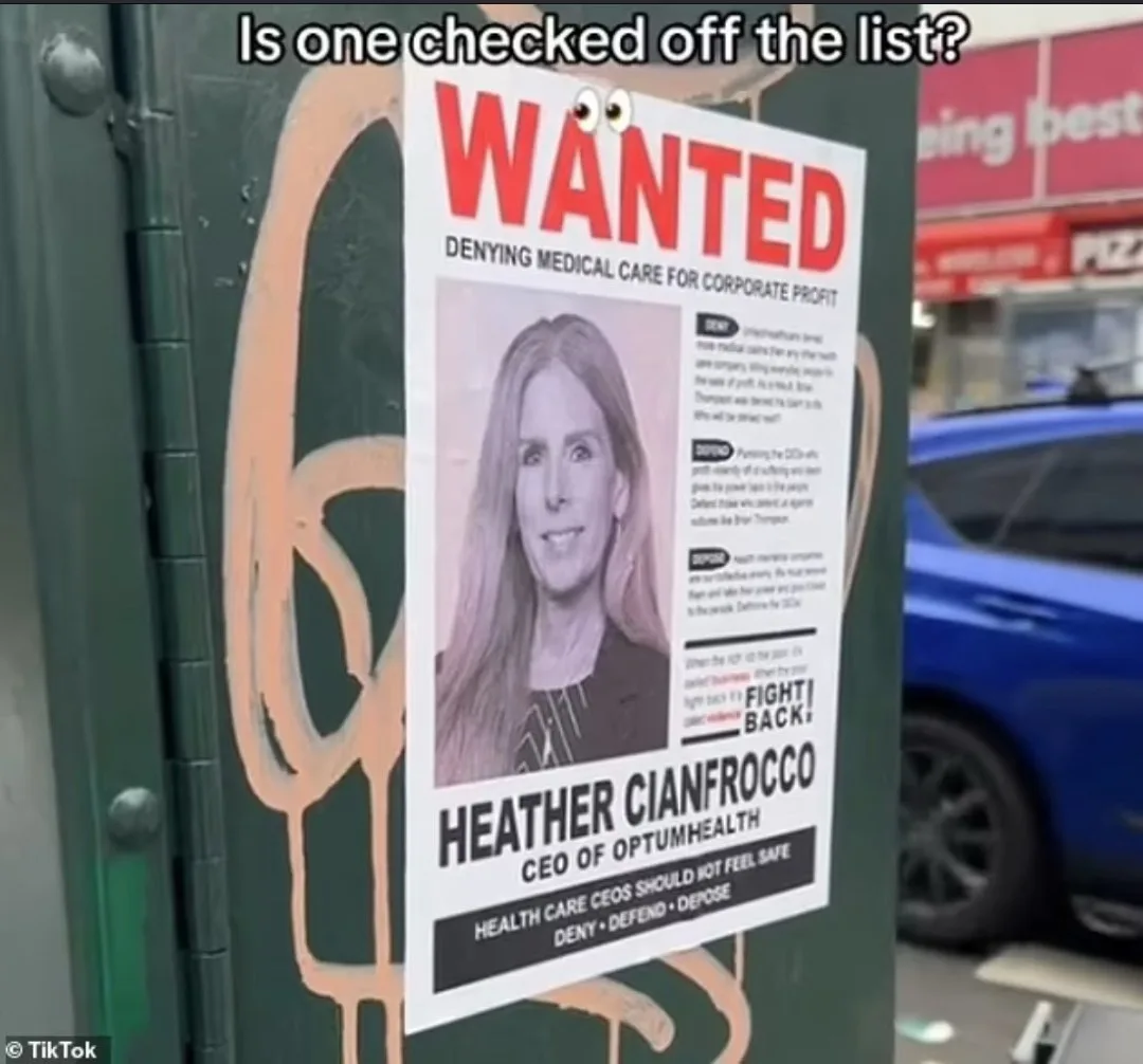A 'WANTED' poster featuring a photo of Heather Cianfrocco, CEO of OptumHealth, is taped to a green metal surface with orange…