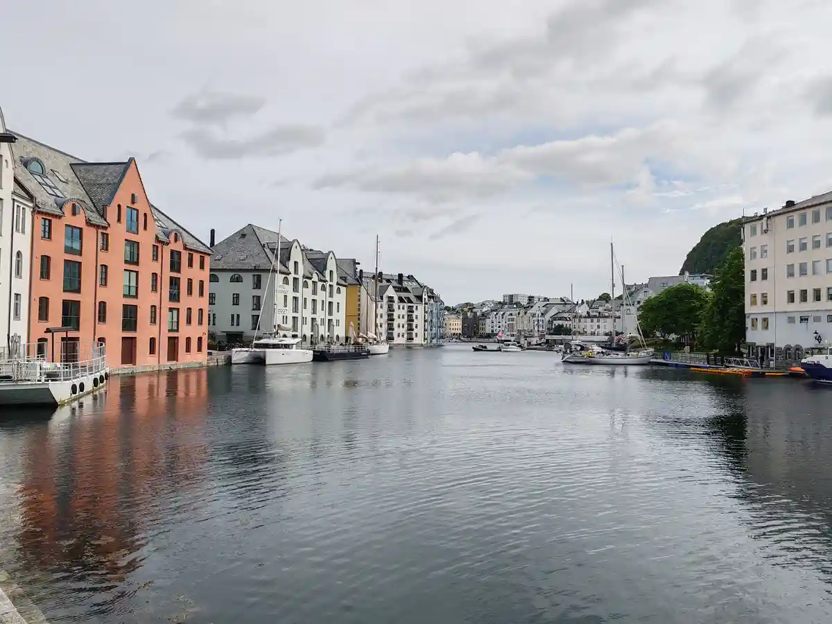 A scenic view of a calm harbor with colorful buildings lining both sides, boats docked along the water, and a cloudy sky…