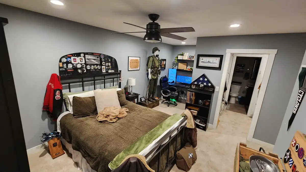A bedroom is filled with military-themed decor, including a mannequin in a green uniform, an airplane cockpit panel…