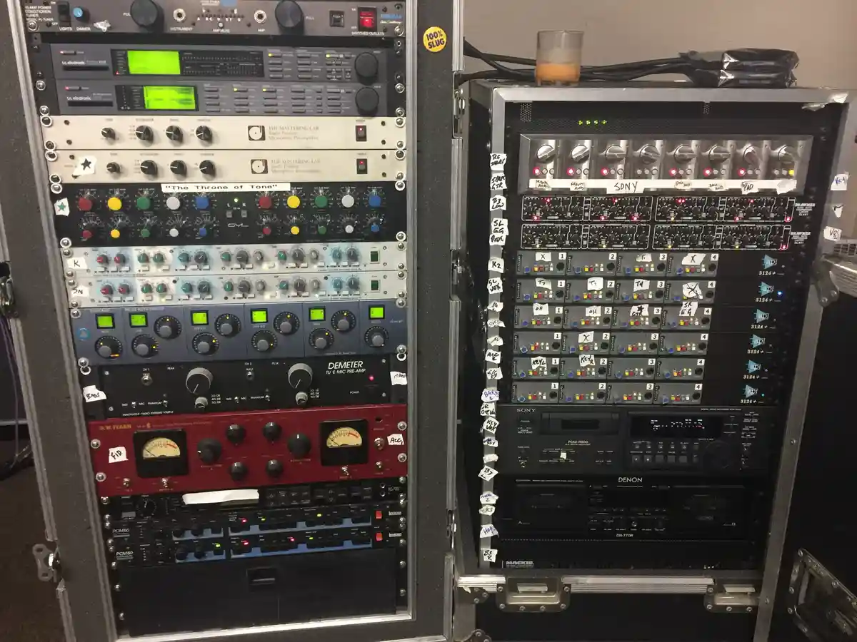 Two tall racks of professional audio equipment are shown side by side, densely packed with knobs, buttons, and glowing…