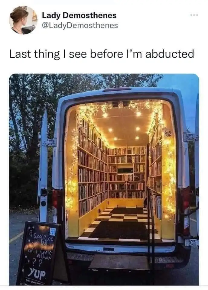 A white van's rear doors are open, revealing an interior transformed into a cozy, book-filled library with string lights and…
