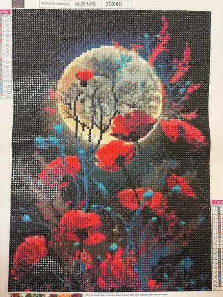 A diamond painting of a skull with red poppies and blue stems, made from tiny colored beads, shows a partially completed…