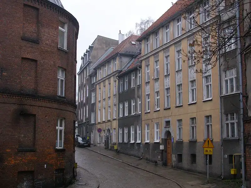 a narrow cobblestone street lined with old European-style buildings, including a prominent curved brick structure on the…