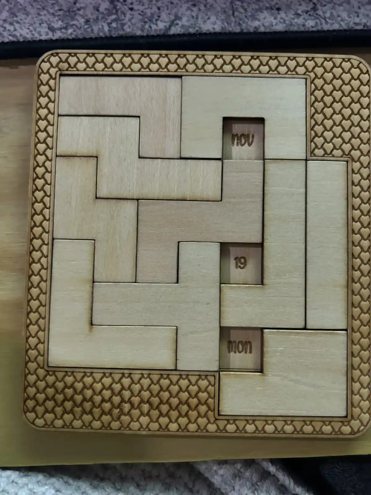 A wooden puzzle calendar with interlocking pieces forming a grid, three small pieces are engraved with 'nov', '19', and…