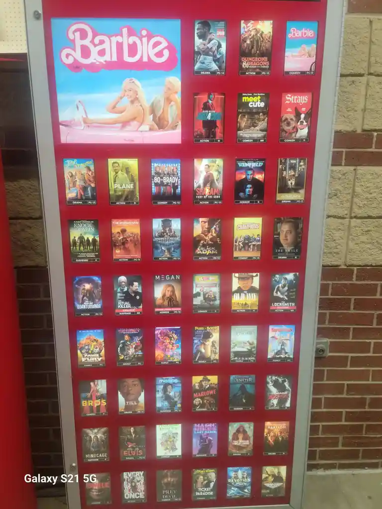 A red movie theater marquee displays numerous movie posters, with the top-left poster for 'Barbie' prominently featuring its…