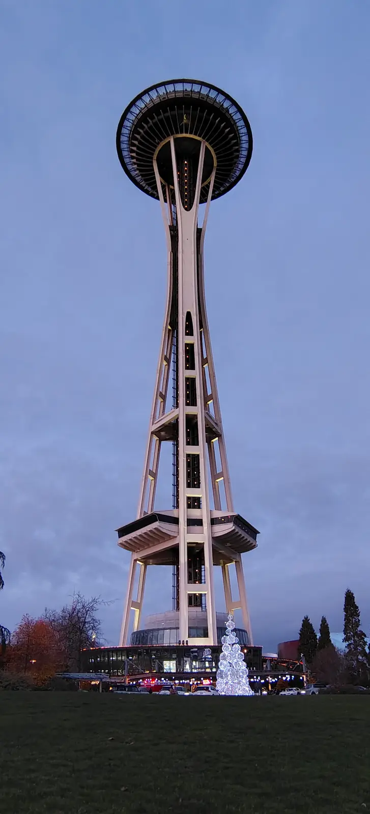 A low-angle photo of the Seattle Space Needle at dusk, with its iconic saucer top and supporting legs illuminated against a…