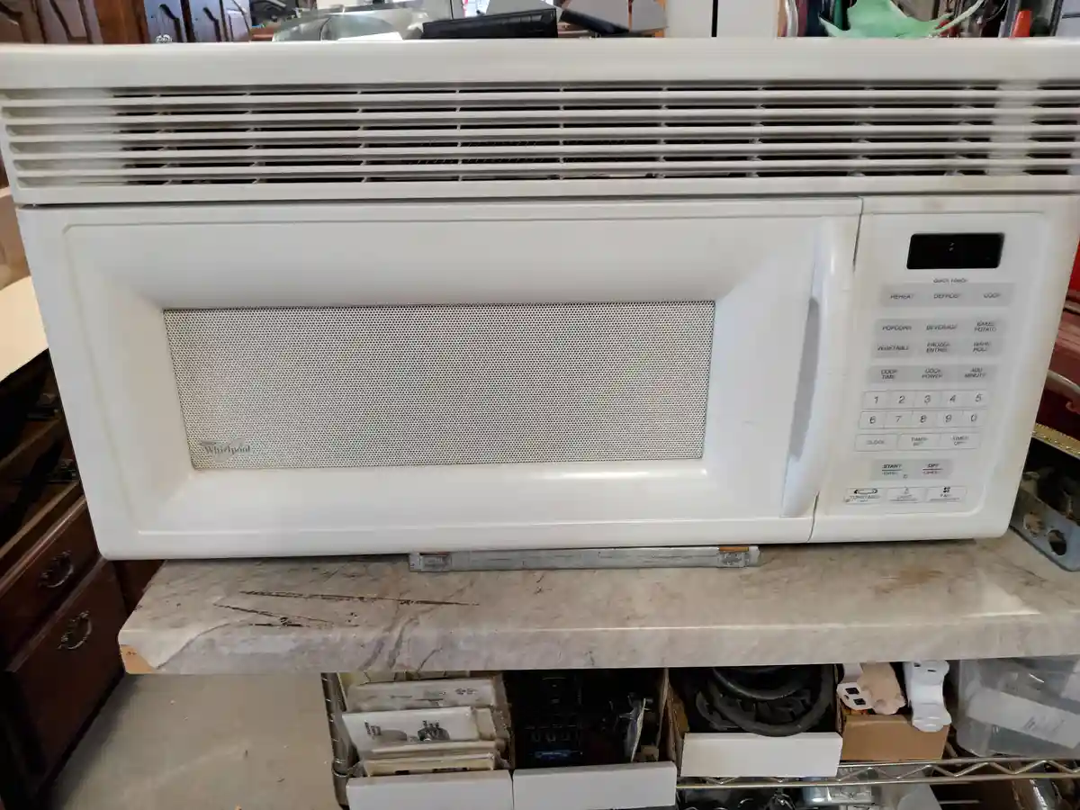 A white Whirlpool microwave oven sits on a marble countertop, its control panel visible with buttons for functions like…