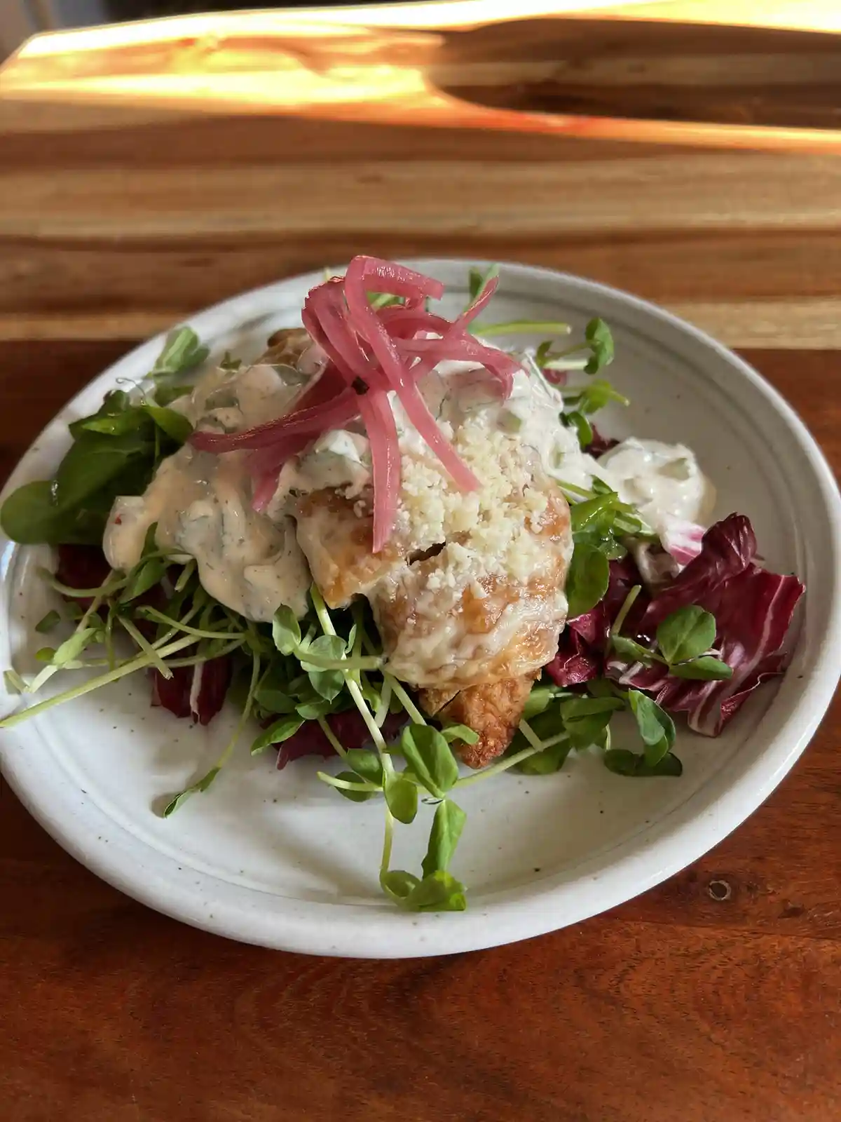 A close-up photo of a plated dish featuring a piece of breaded and fried chicken atop a bed of mixed greens, including…