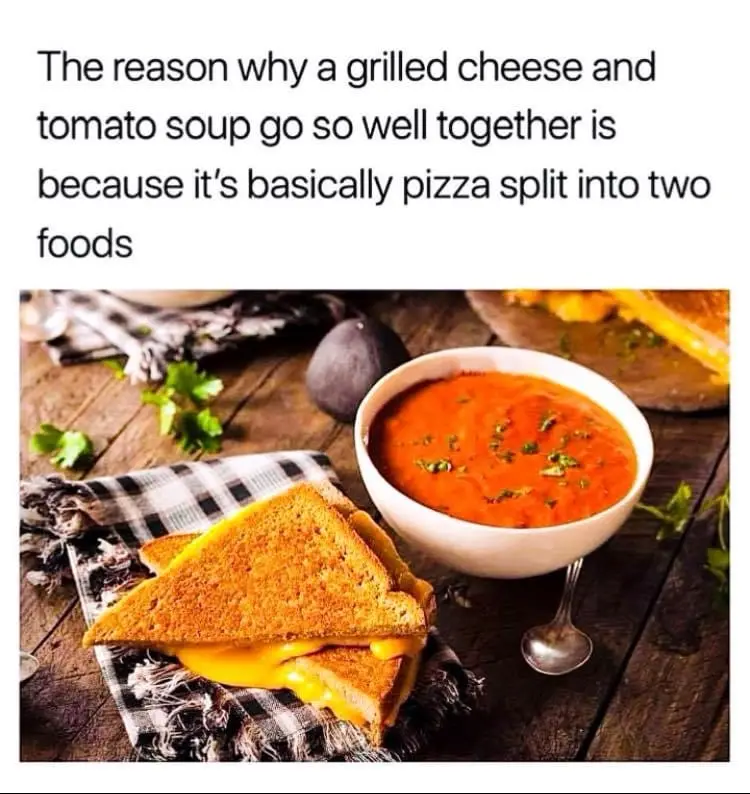 A grilled cheese sandwich with melted cheese oozing out sits next to a bowl of tomato soup garnished with herbs on a wooden…