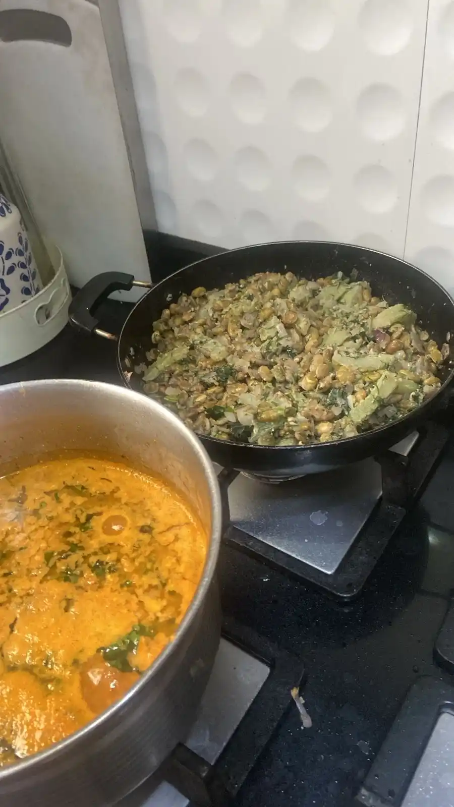A kitchen stove with two pots: one contains a simmering orange curry, the other a green vegetable dish. Overlaid text reads…