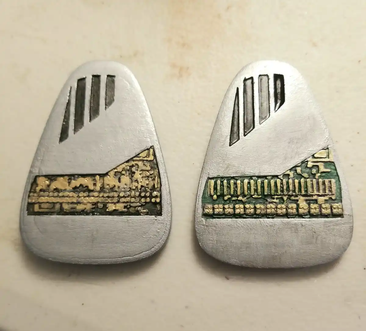 Two silver-colored, teardrop-shaped objects sit side by side on a light surface. Each has three vertical slits near the top…