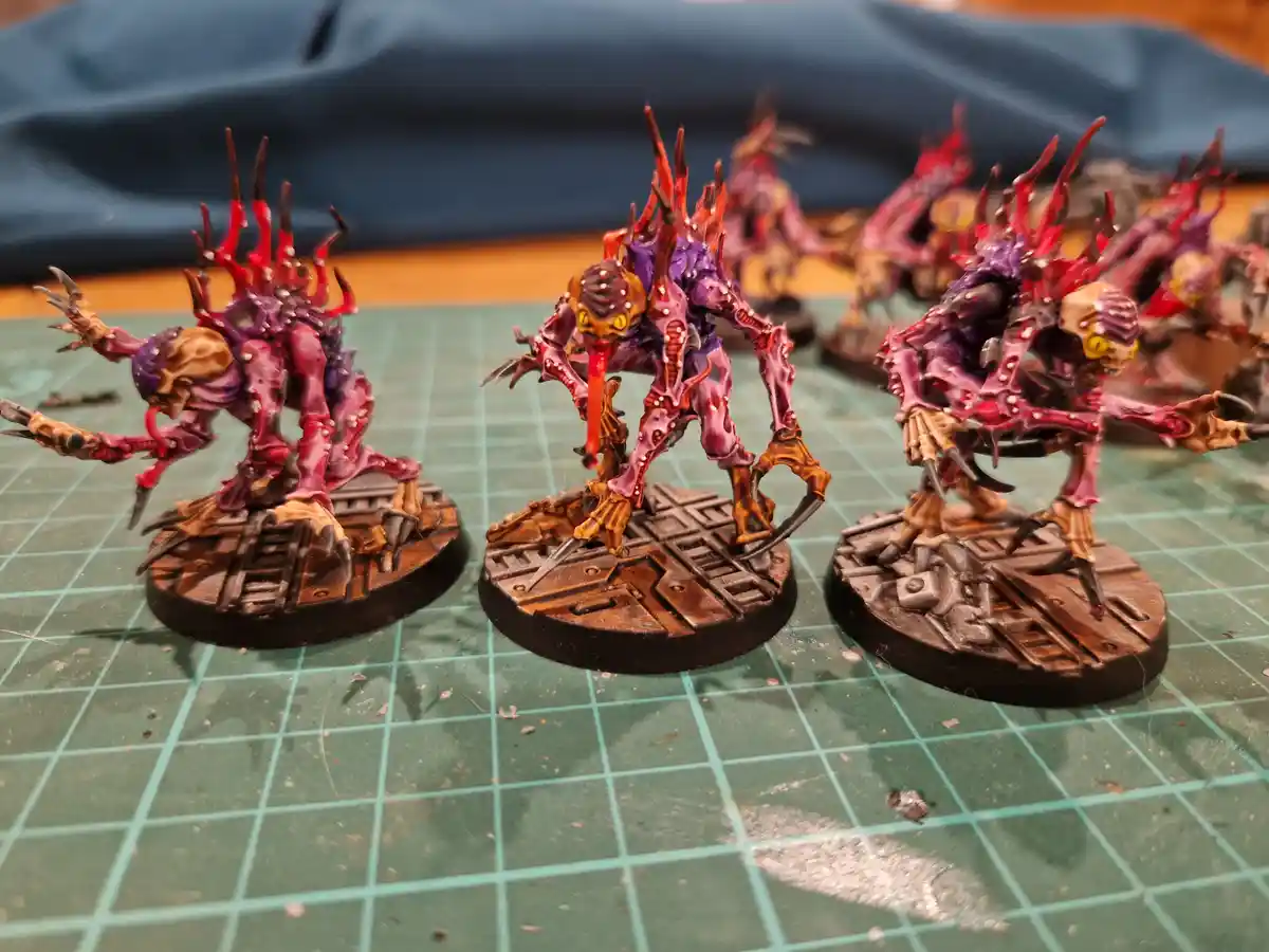 Three intricately painted, grotesque fantasy miniatures with spiky red and purple bodies, yellow eyes, and long tongues…