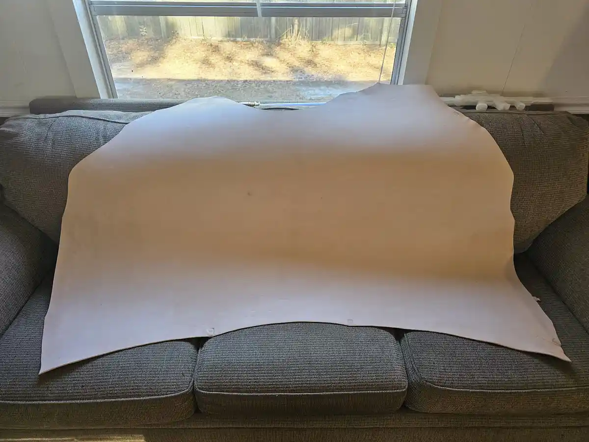 A large, plain white sheet or tarp is draped over a gray fabric couch, covering most of its seating area. The couch is…