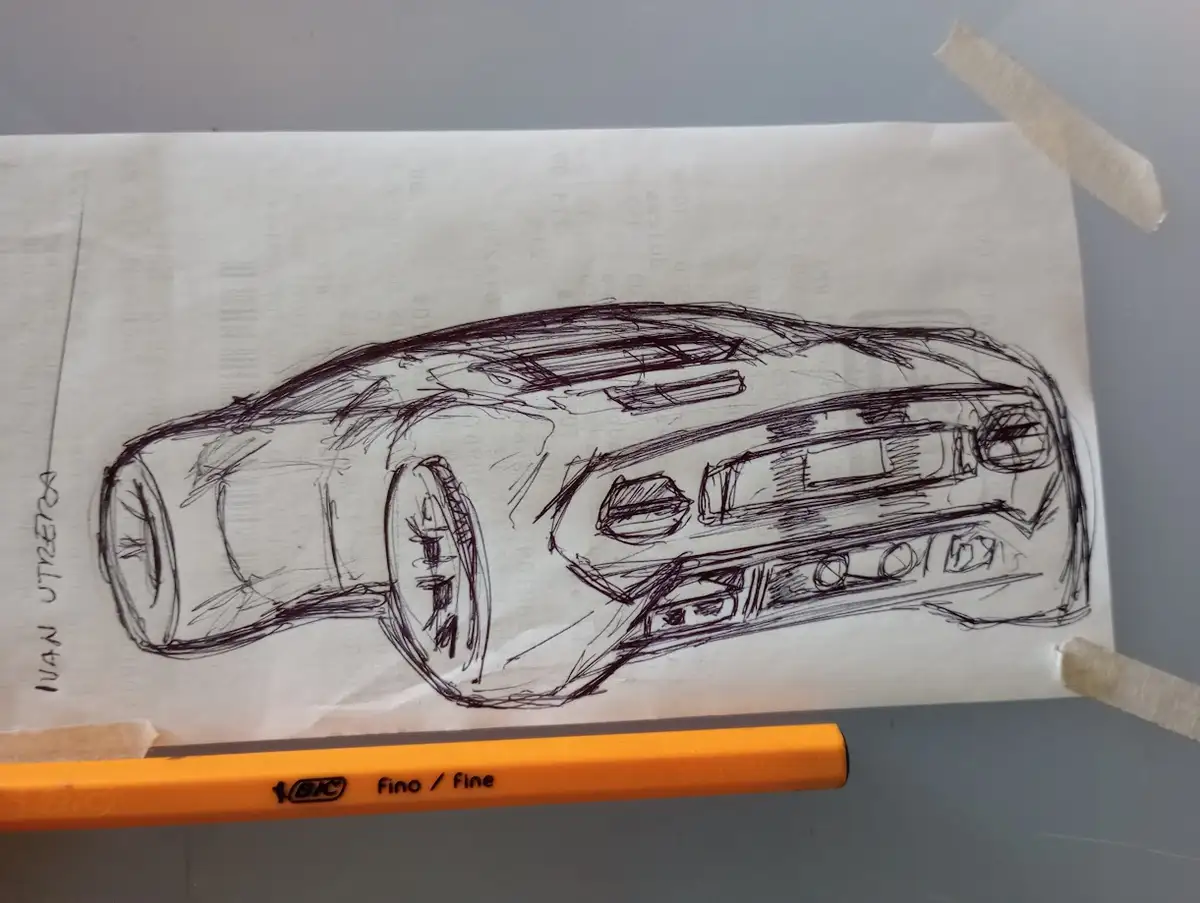 A rough, hand-drawn sketch of a futuristic-looking car on paper taped to a surface, with an orange BIC fine pencil lying in…