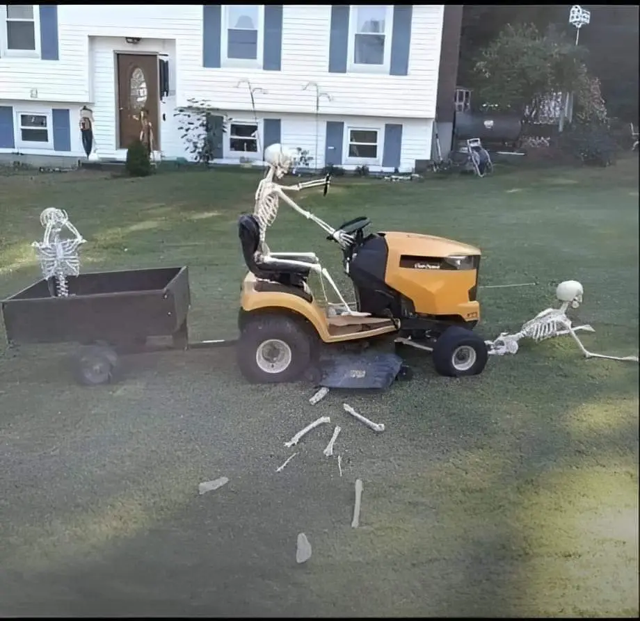 A yellow riding lawn mower with a skeleton driver and a skeleton hitched to the back, pulling a trailer with another…