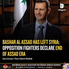 A man in a dark suit and tie smiles while standing in front of a Syrian flag. Overlaid text in bold yellow and white reads…