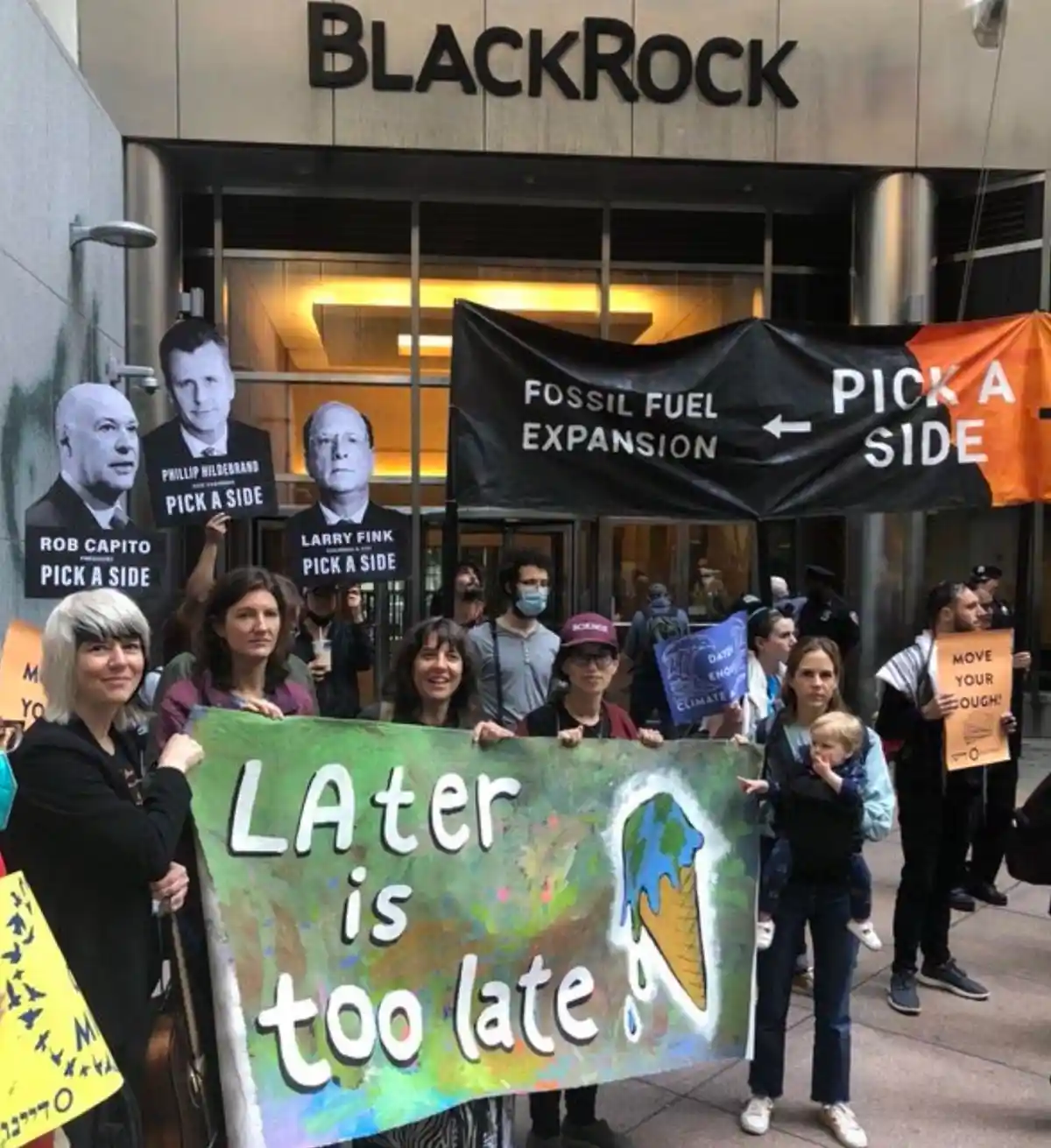 A group of climate activists protest outside a BlackRock building, holding signs with the names of executives like Larry…