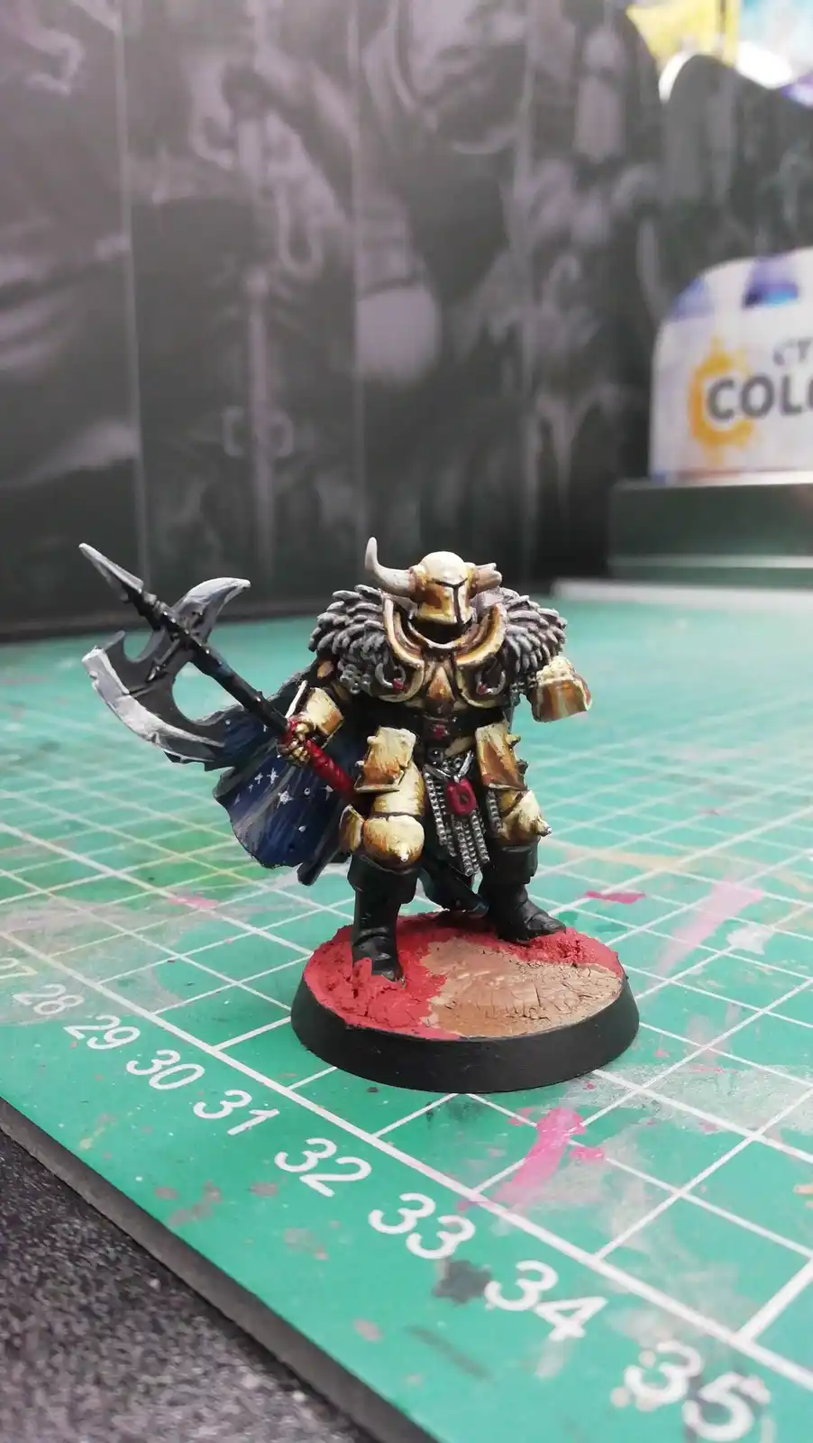 A painted miniature of a fantasy warrior with horns, wielding a large axe and wearing ornate armor, stands on a circular…