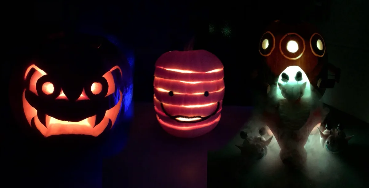 Three carved pumpkins glow in a dark room: a traditional scary jack-o'-lantern on the left, a smiling pumpkin with…