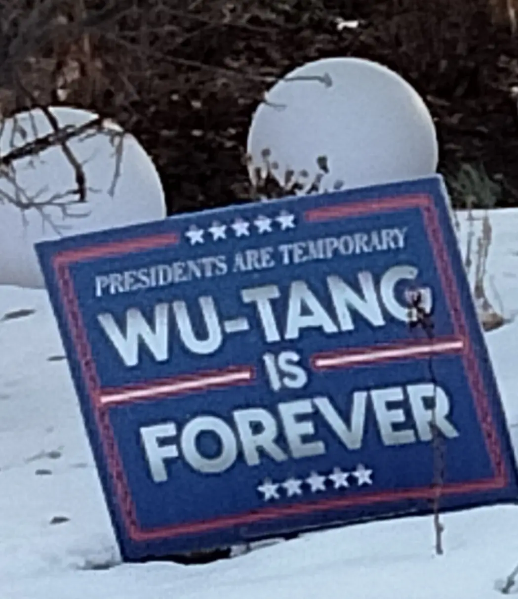 A blue political-style yard sign with red trim and white text reading 'PRESIDENTS ARE TEMPORARY WU-TANG IS FOREVER' is stuck…