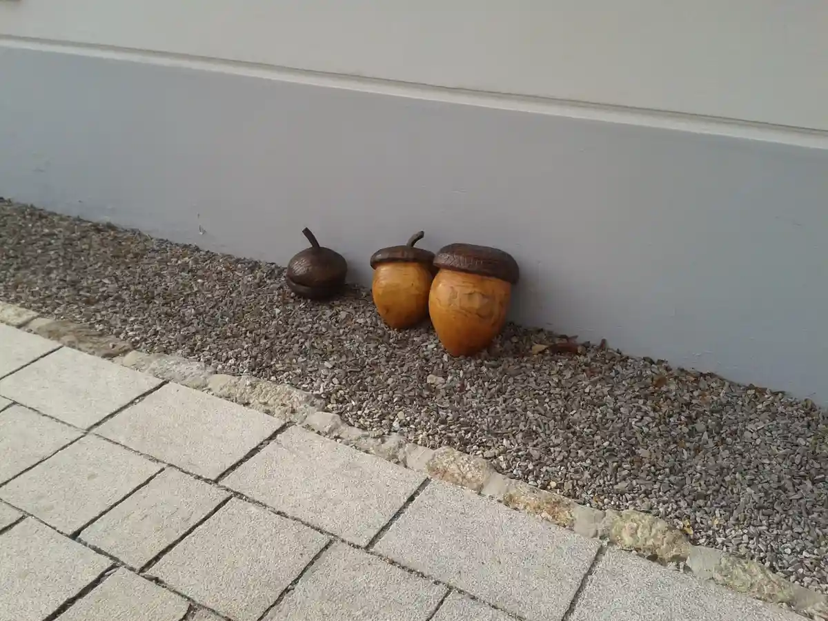 Three decorative acorns sit on gravel next to a wall, with the smallest one on the left appearing to be a fake or hollow…