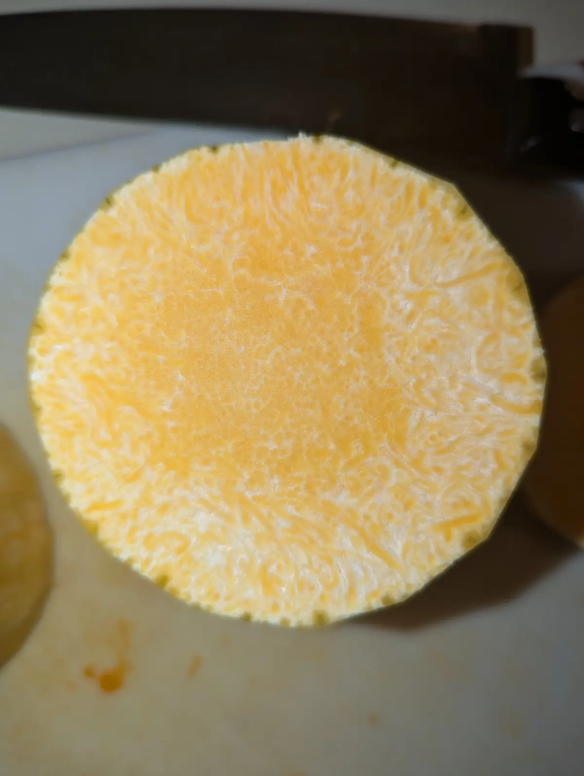 A close-up photo shows a circular cross-section of a sweet potato on a white cutting board, revealing its vibrant orange…