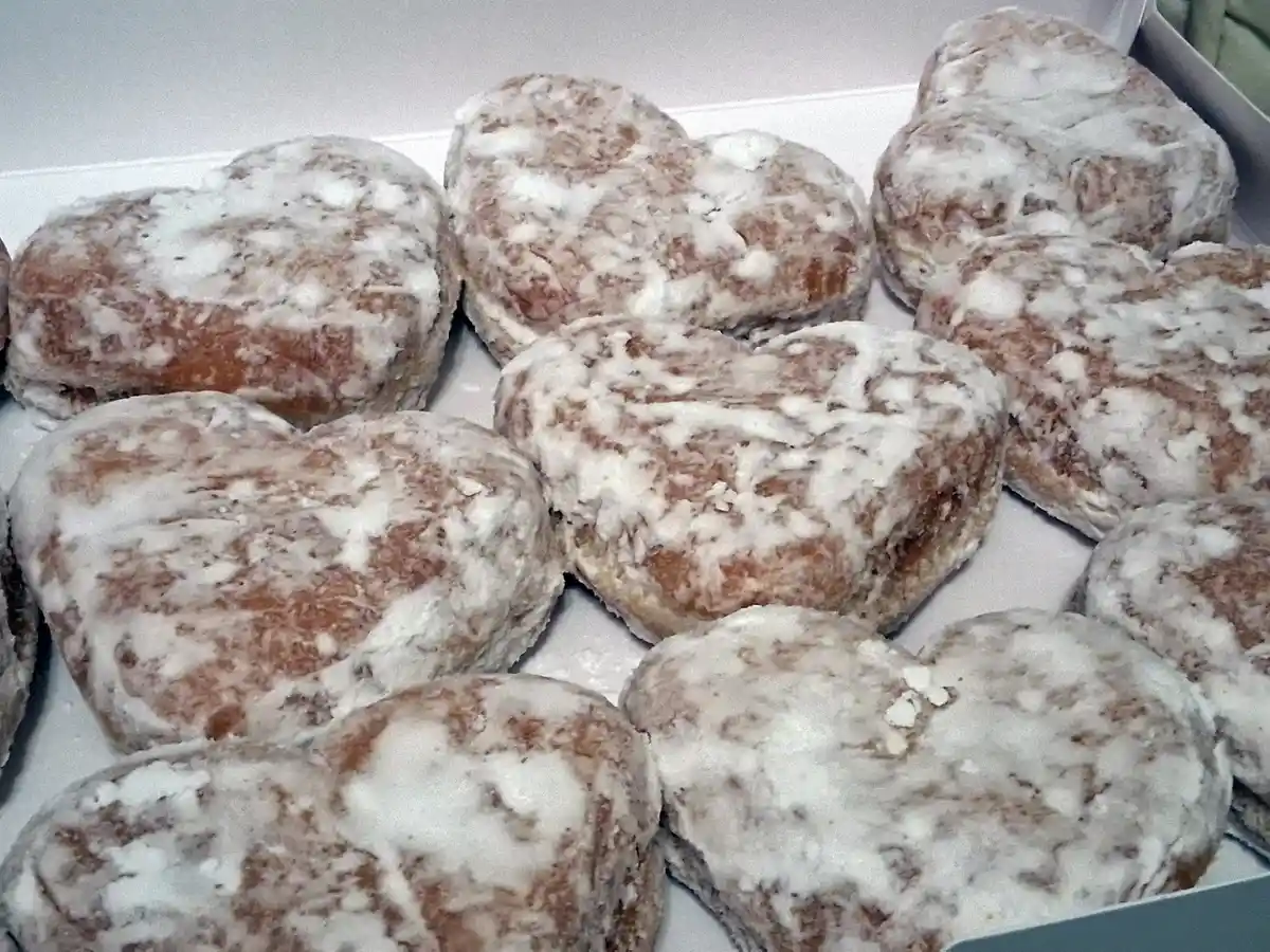 A box filled with heart-shaped, sugar-coated donuts, each covered in a thick, uneven white glaze. The overlaid text reads 'i…