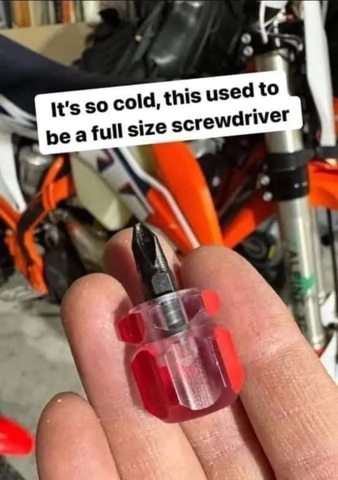A hand holds a tiny, red, translucent plastic screwdriver with a black bit, humorously implying it was once full-sized due…
