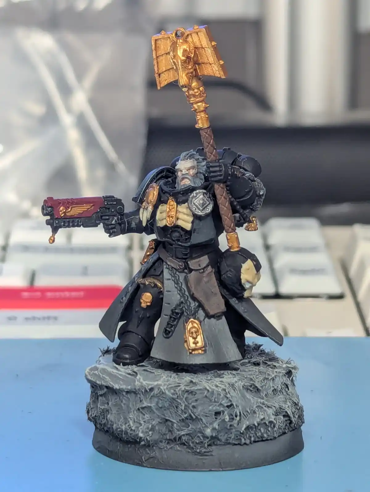 A heavily detailed, painted miniature of a grimdark fantasy warrior, likely from Warhammer 40,000, stands on a rocky base…