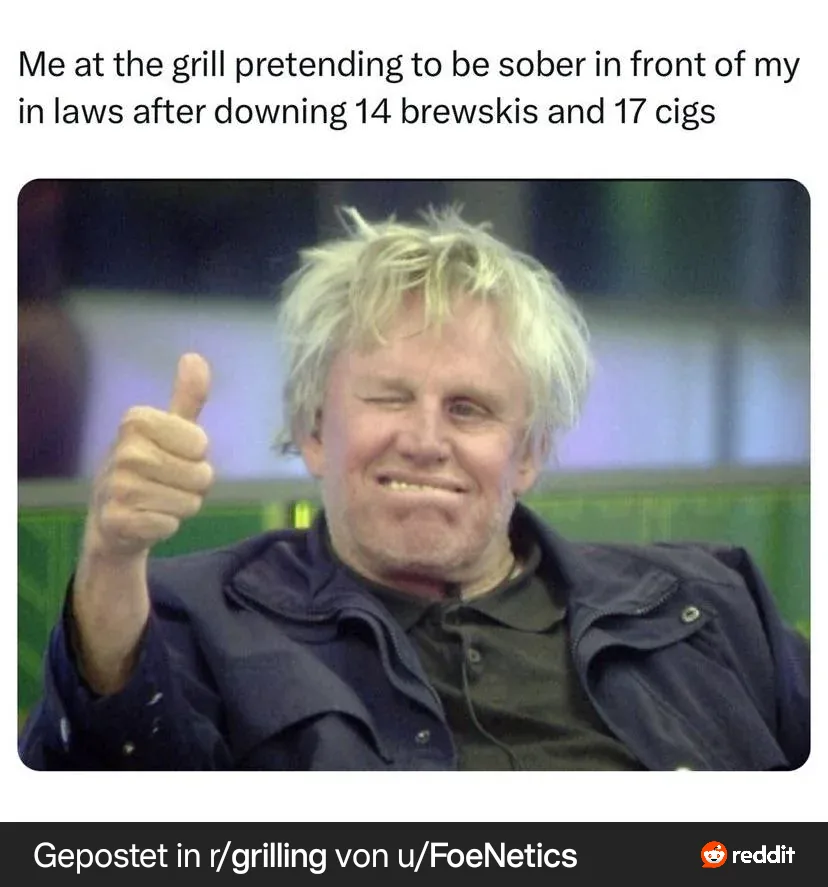 A man with messy blonde hair, wearing a dark jacket over a dark shirt, gives a thumbs-up while winking and smiling broadly…