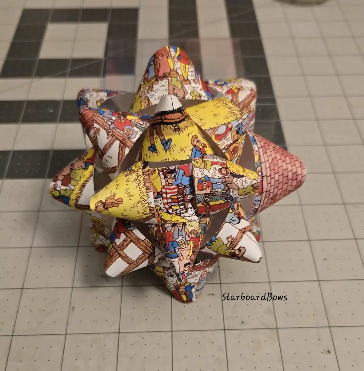 A 3D geometric paper sculpture, resembling a star or polyhedron, is constructed from panels printed with colorful…
